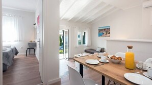 Una habitación moderna con una mesa de madera dispuesta para el desayuno, un sofá y una cama con vistas al exterior.