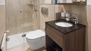 Un baño moderno con ducha separada por mampara de vidrio, inodoro blanco y tocador de madera oscura con espejo.
