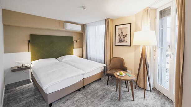 Habitación de hotel con cama, una silla, una mesa, lámpara y ventana con cortinas.