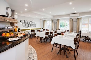 A hotel dining area with multiple tables, a buffet with fruits and beverages, and framed pictures on the wall. - Hotel Löwen Am See (Zug)