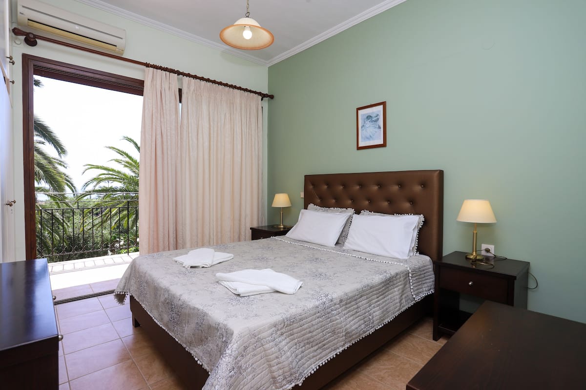 Un dormitorio con cama, dos mesitas de noche con lámparas, una ventana con cortinas e imagen en la pared.