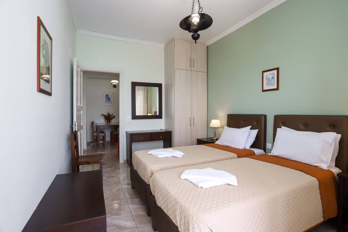 Habitación de hotel con dos camas, un escritorio, una silla, un armario y un área de comedor.