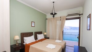 Quarto de hotel com duas camas, varanda com vista, luminária pendente e aparelho de ar condicionado.
