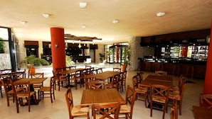 Un comedor amplio con mesas y sillas de madera, una zona de bar con estantes llenos de botellas y un pilar de piedra.