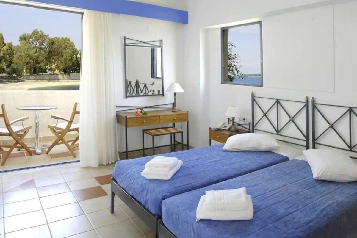 A hotel room with two beds, a desk, a chair, a window, and a view of the beach.