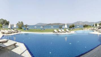 Una piscina amb gandules i ombrel·les, envoltada de vegetació i vista al mar.