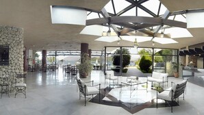 Un vestíbulo amplio con una zona de estar central, paredes de piedra y grandes ventanales con vistas al exterior.