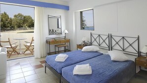 Habitación de hotel con dos camas, un escritorio, una silla, ventana con vistas y balcón con mesa y sillas.