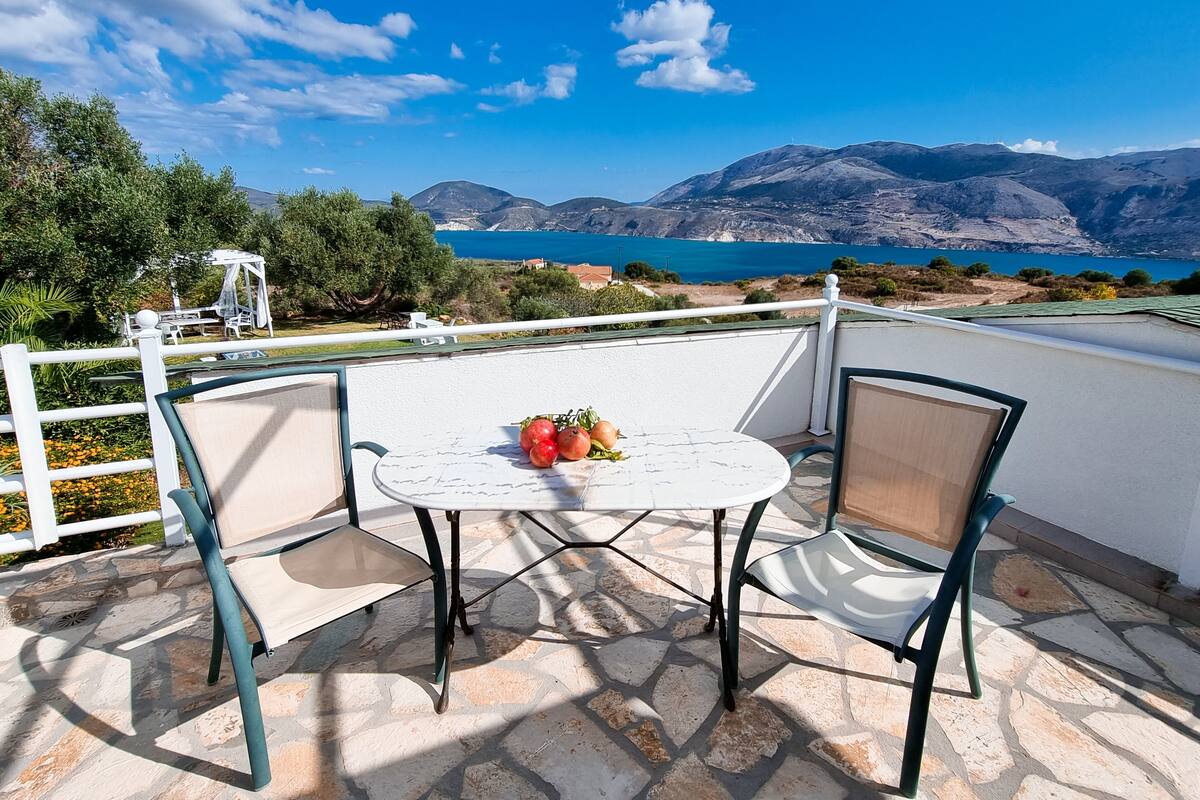 Una terraza con mesa y sillas, vista al mar y a las montañas, y una valla blanca.