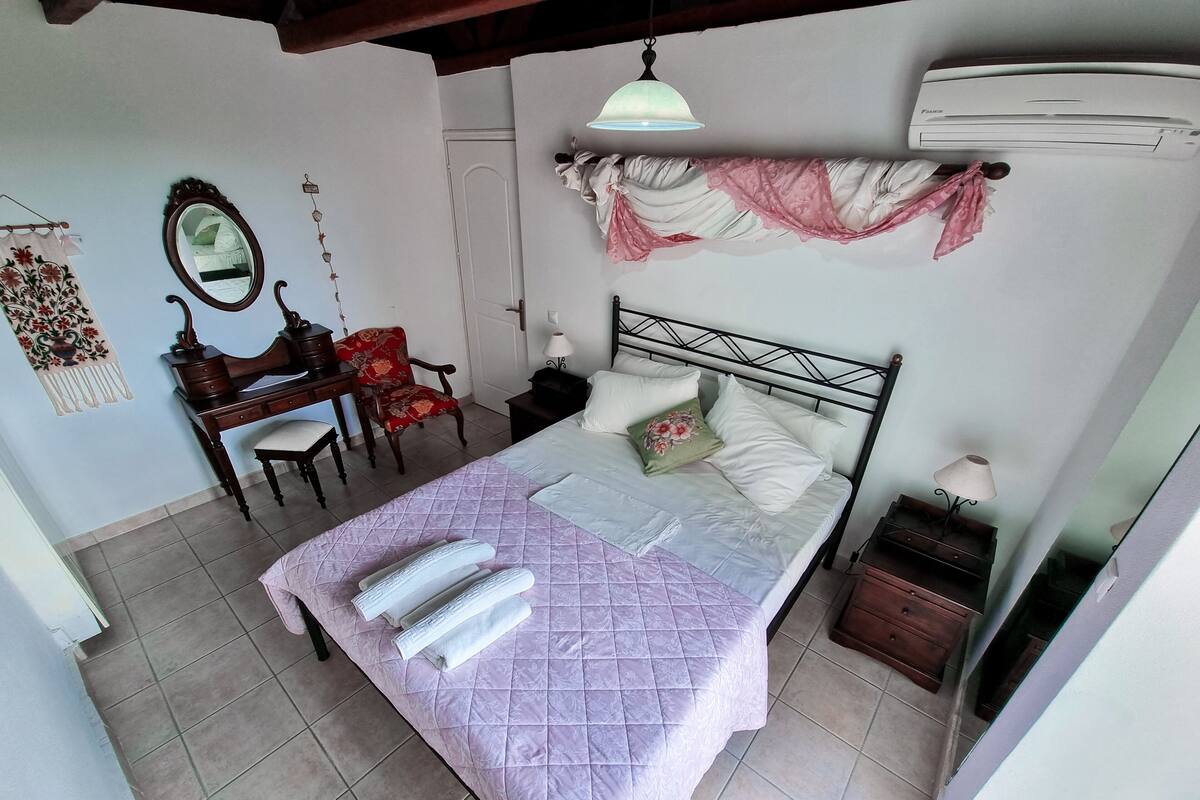 Un dormitorio con cama, escritorio, silla, espejo y aire acondicionado.