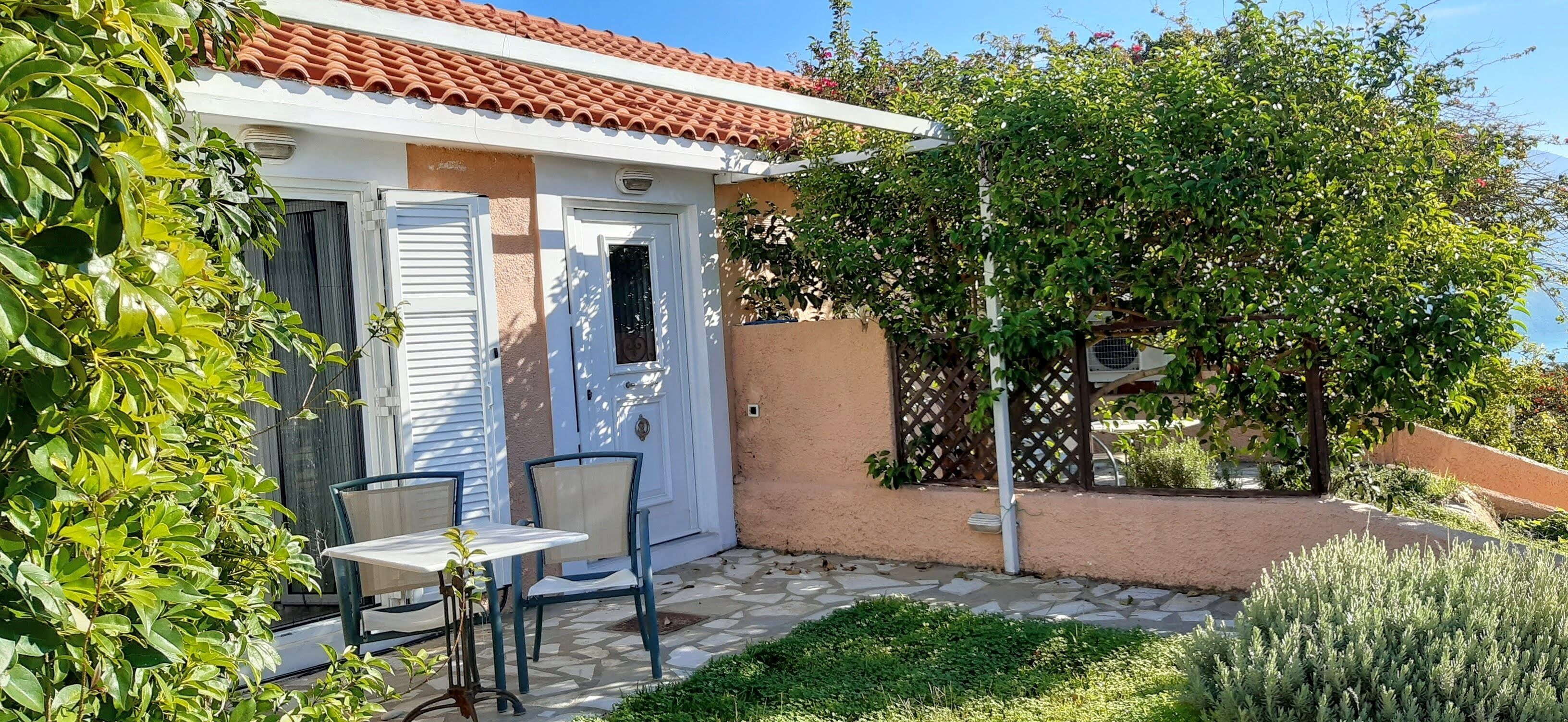 A house with a tiled roof, a white door, and a small patio with a table and chairs.
