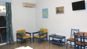 A room with two yellow armchairs, a small table, a dining table with chairs, a TV, and a window with curtains. - Agnanti Studios (Kefalonia)