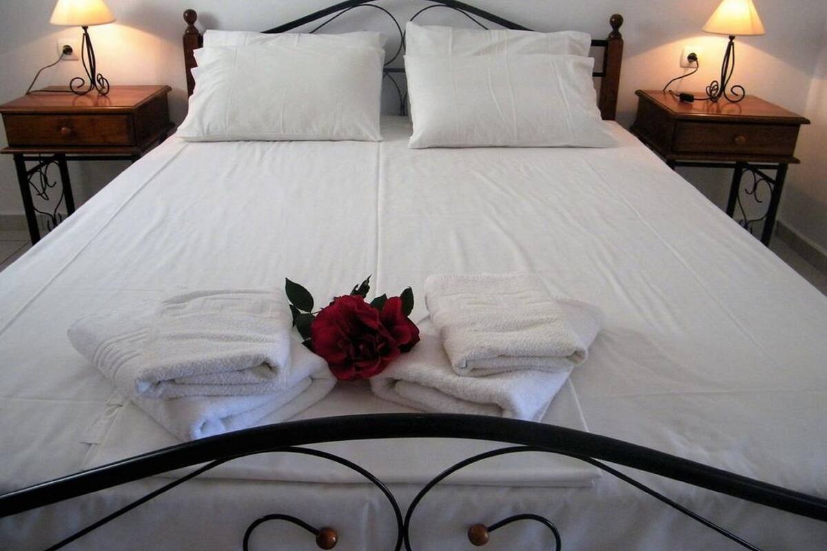 Un lit double avec du linge de lit blanc, deux tables de chevet avec des lampes et une rose rouge décorative posée sur le lit.