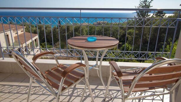 A balcony with a round table and two chairs, overlooking a coastal view. - Agnanti Studios (Kefalonia)