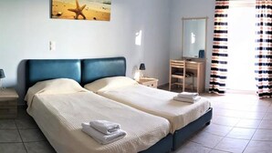 A double bed with a blue headboard, a bedside table with a lamp, a dresser, a mirror, striped curtains, and a small table with a vase. - Agnanti Studios (Kefalonia)