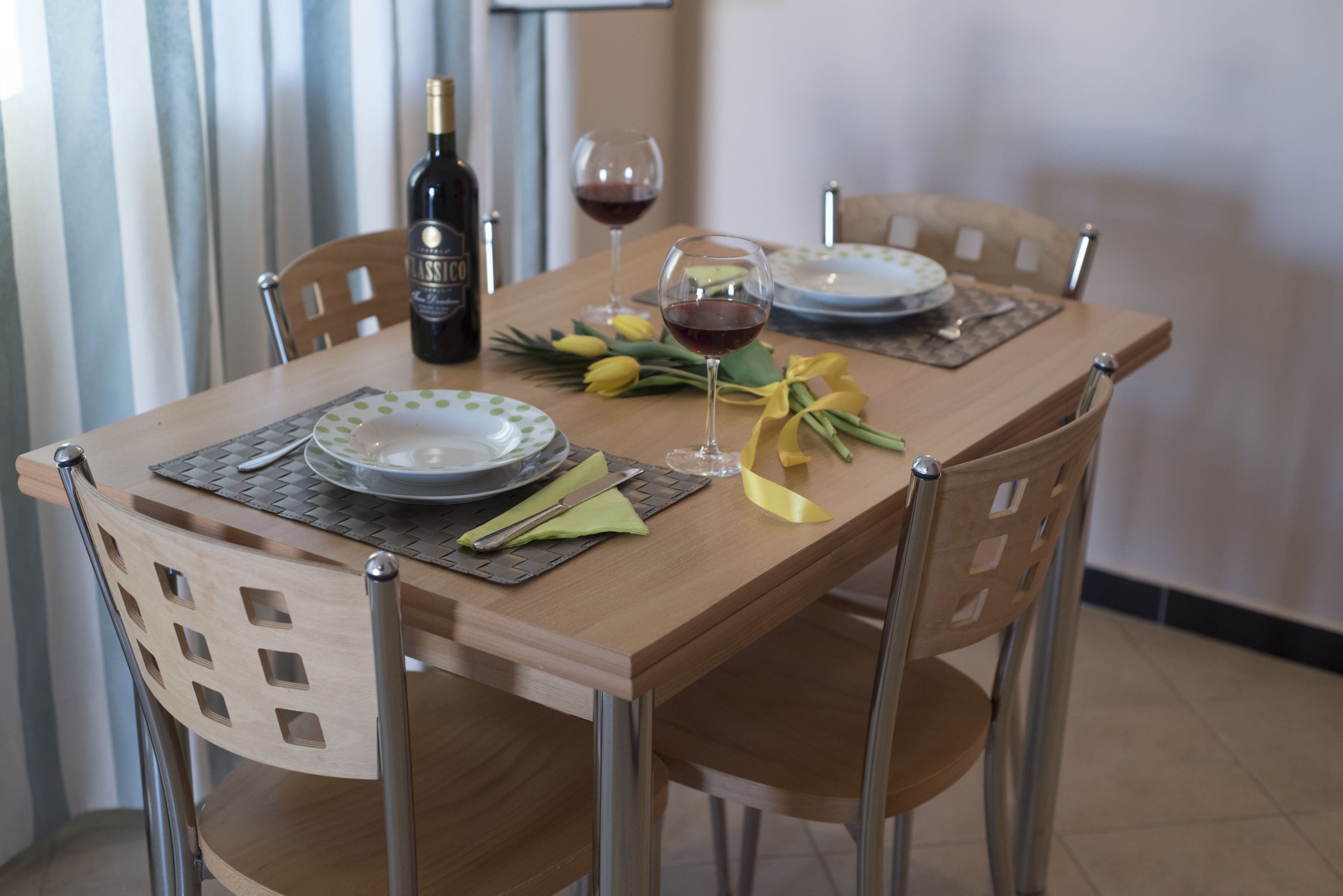 A dining table set with plates, cutlery, a wine bottle, and a glass of red wine.