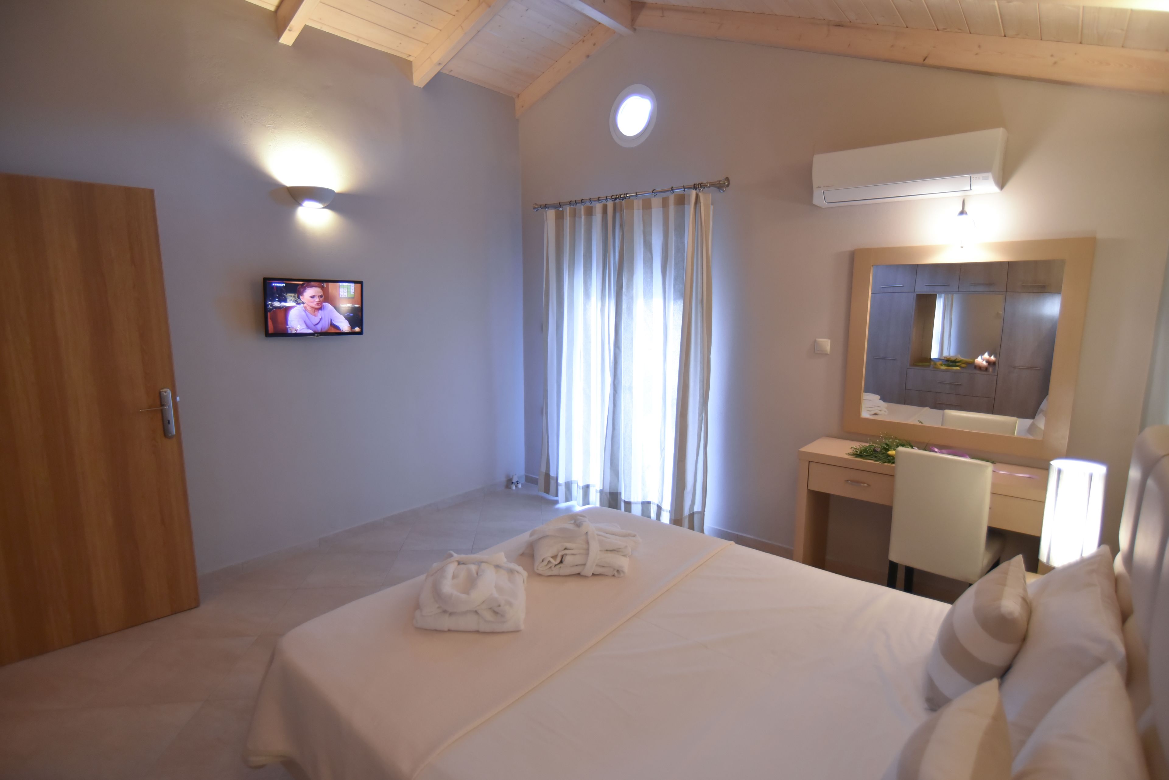 A hotel room with a bed, a desk, a chair, a TV, and a bathroom with a shower curtain.
