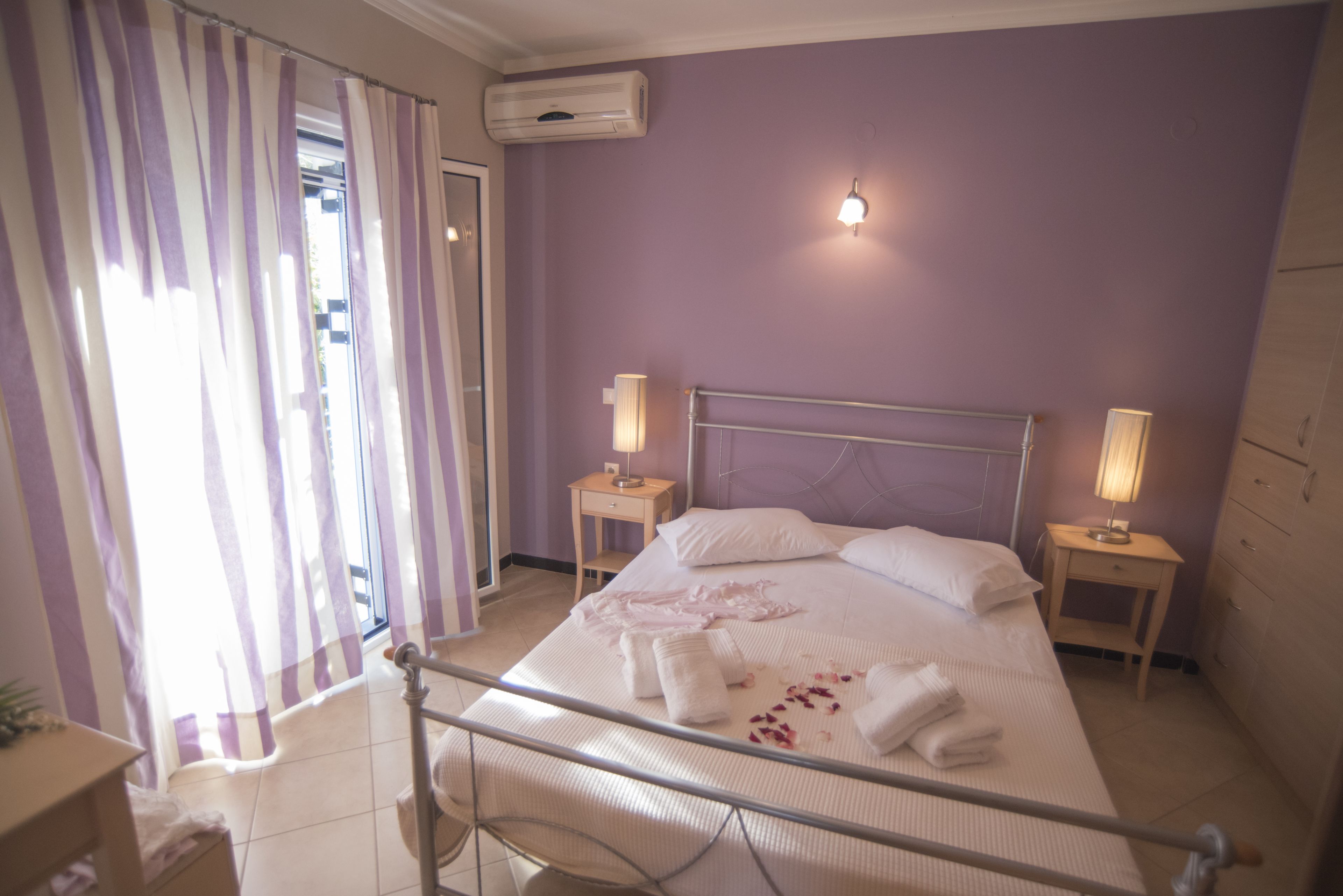 A bedroom with a bed, two bedside tables, a nightstand, a window with curtains, and an air conditioning unit.