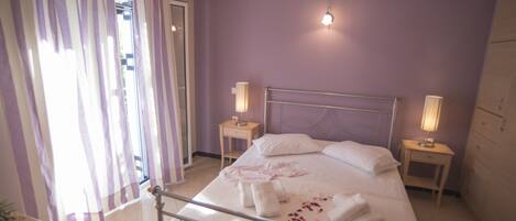 A bedroom with a bed, two bedside tables, a nightstand, a window with curtains, and an air conditioning unit.