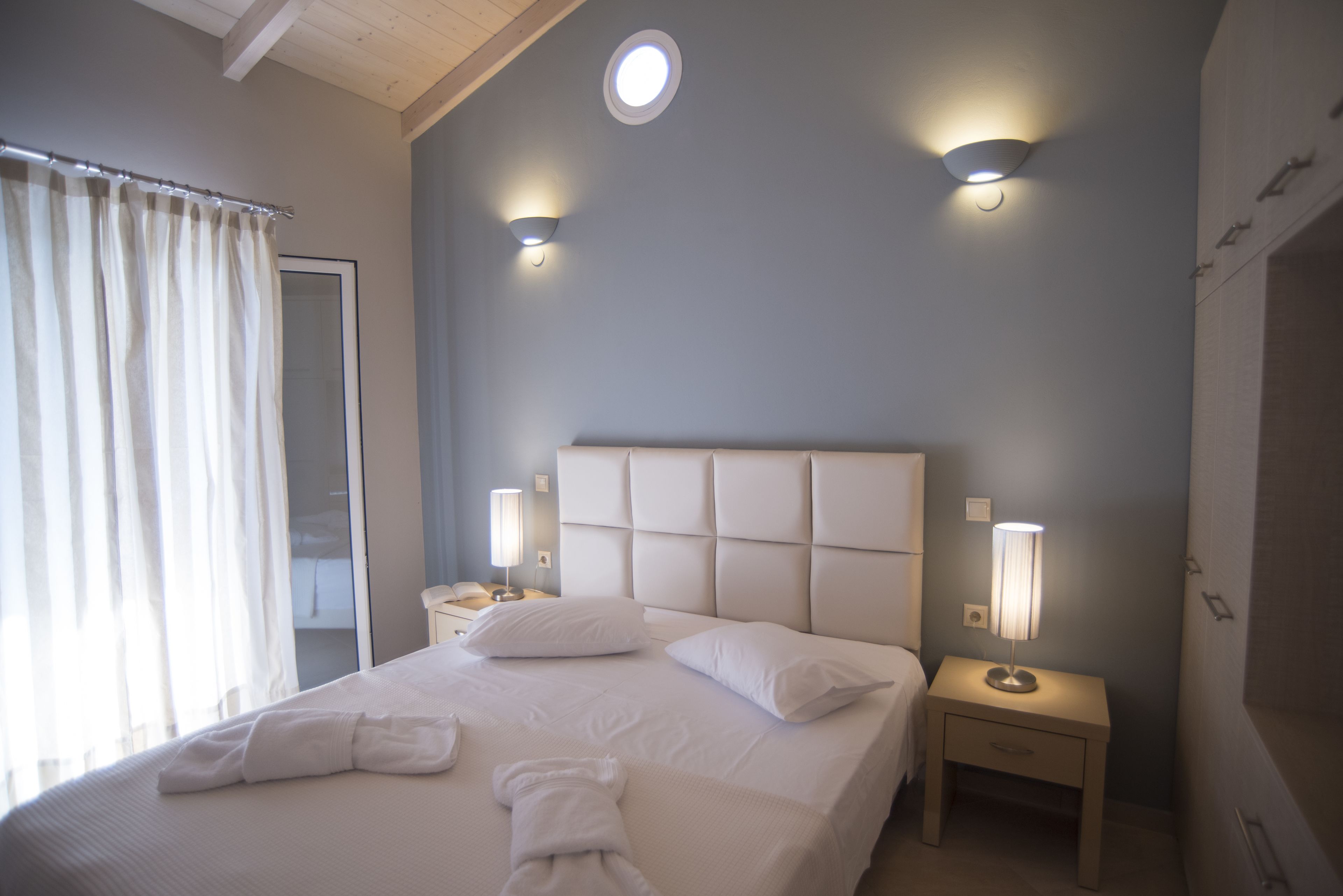 A neatly made bed with white linens and pillows, two bedside lamps, and a headboard.