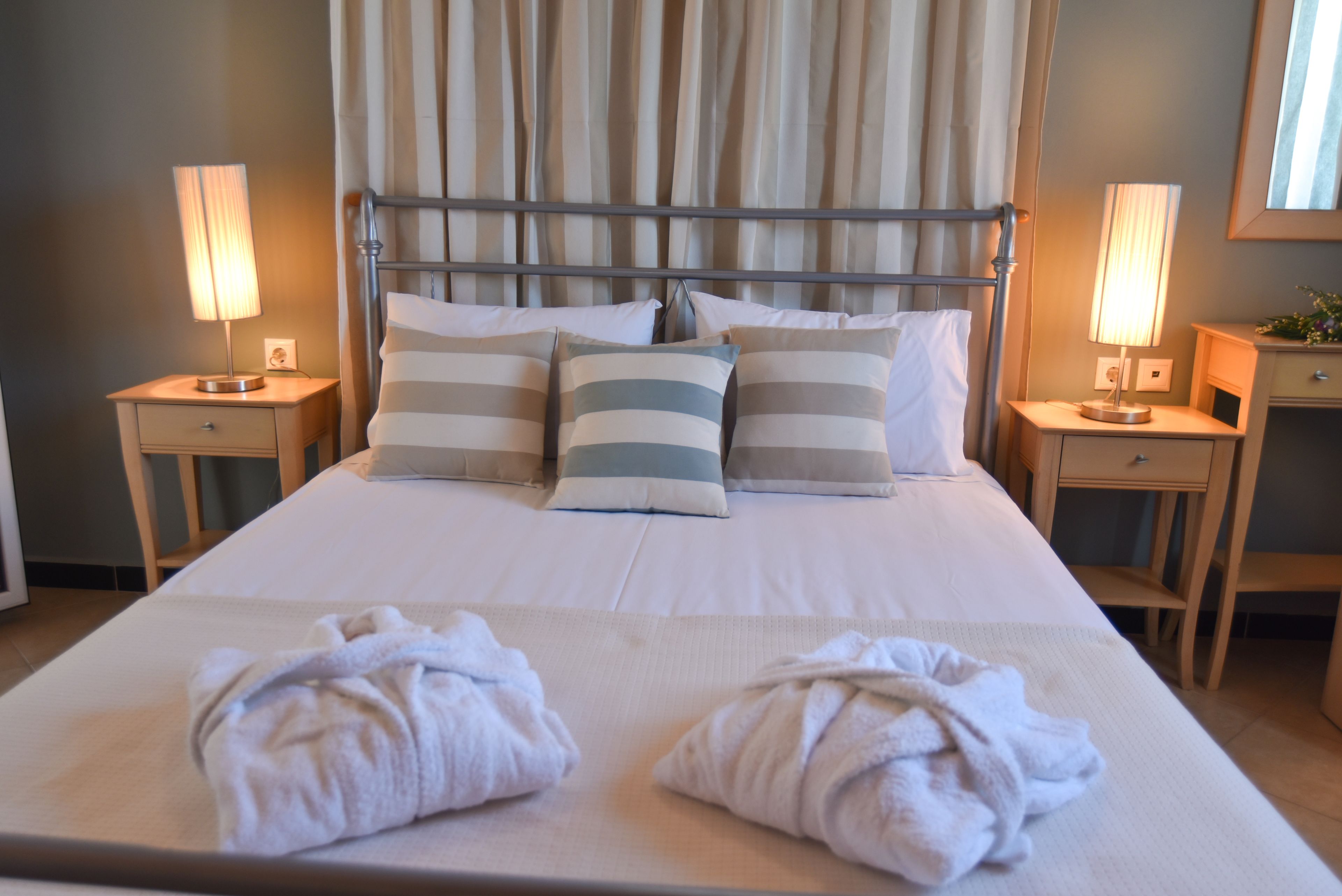 Una cama bien hecha con almohadones a rayas, dos mesitas de noche con lámparas y un espejo grande en la pared.