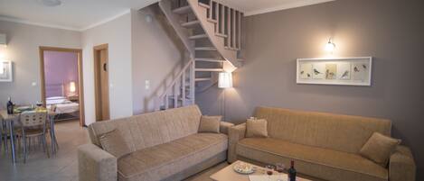 A living room with a beige sofa, a dining table with chairs, and a staircase.