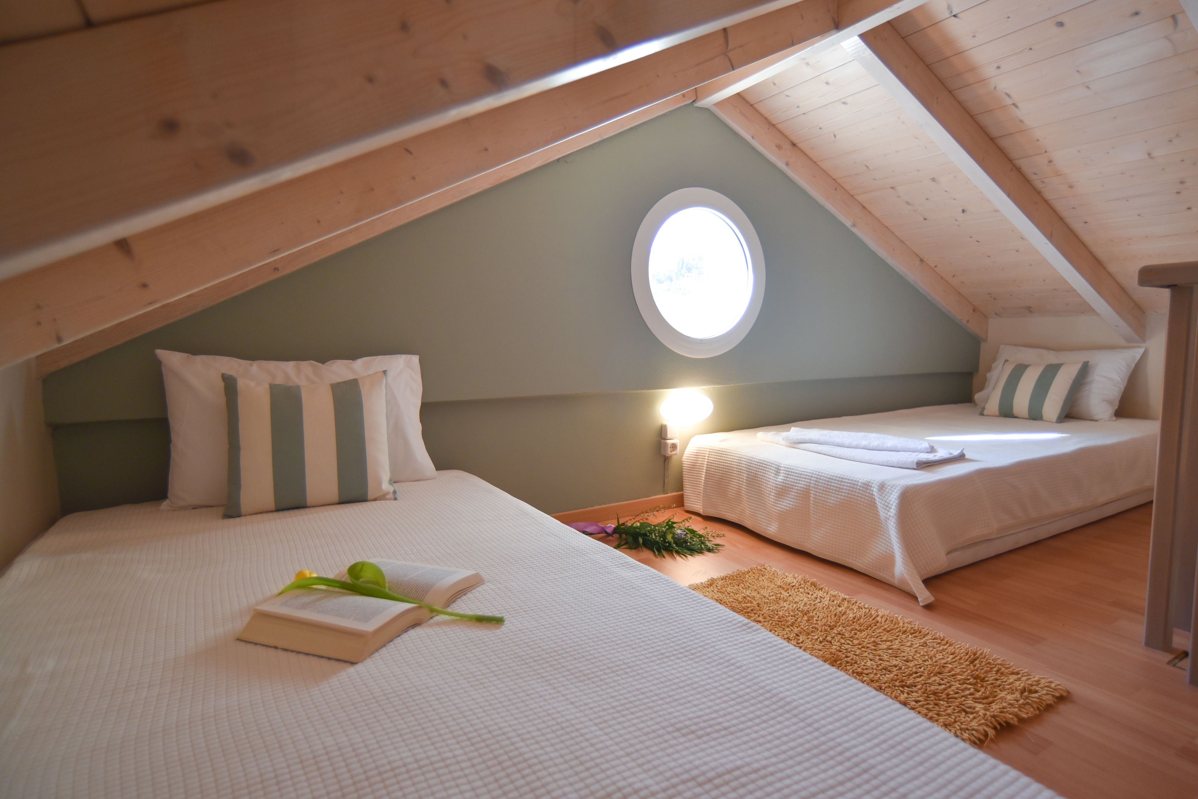 Une chambre mansardée chaleureuse avec deux lits, une petite fenêtre et un plafond en bois.