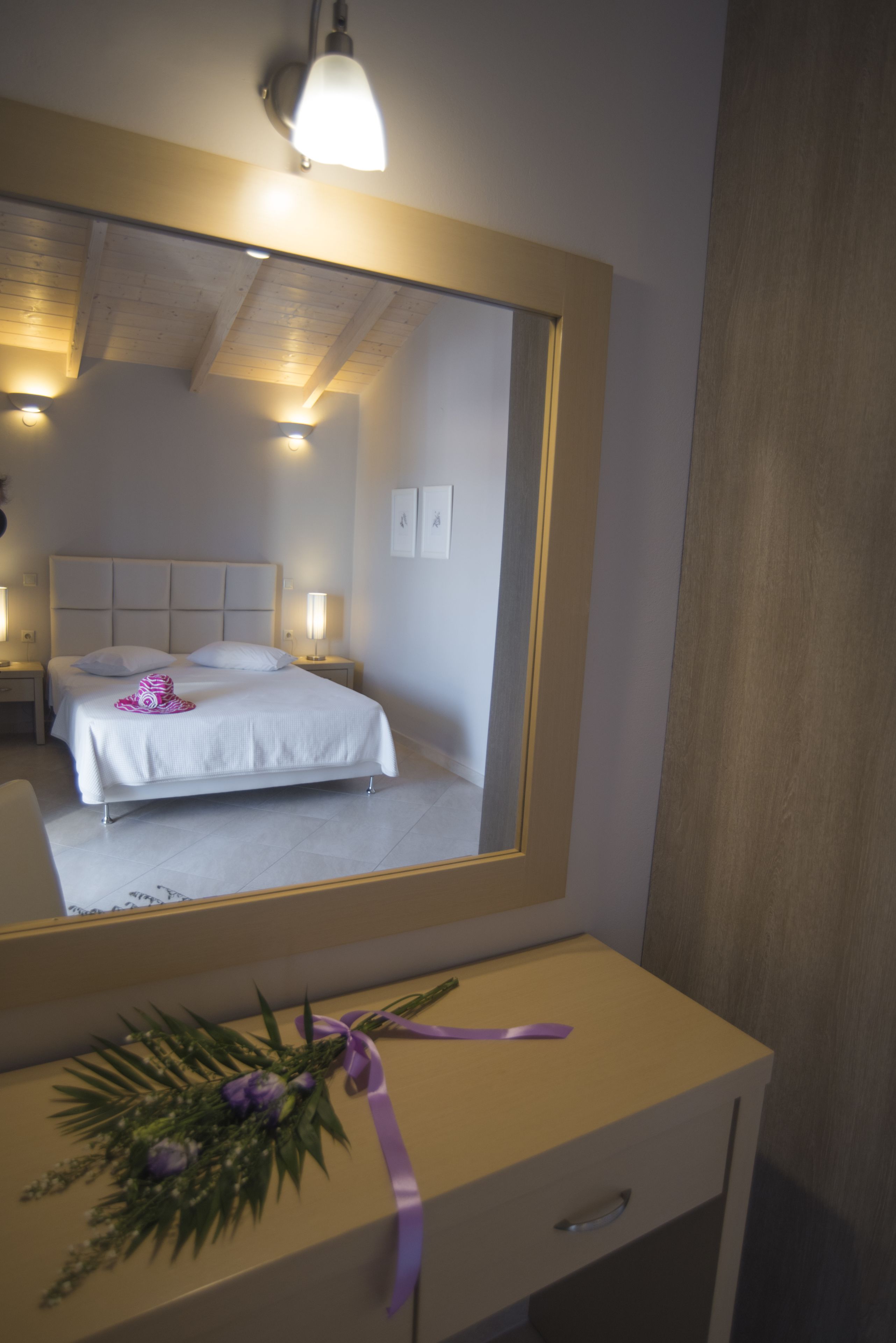 Et hotelværelse med et stort spejl, en seng med hvide sengetøj, et natbord med en lampe og en kommode med et lilla bånd.