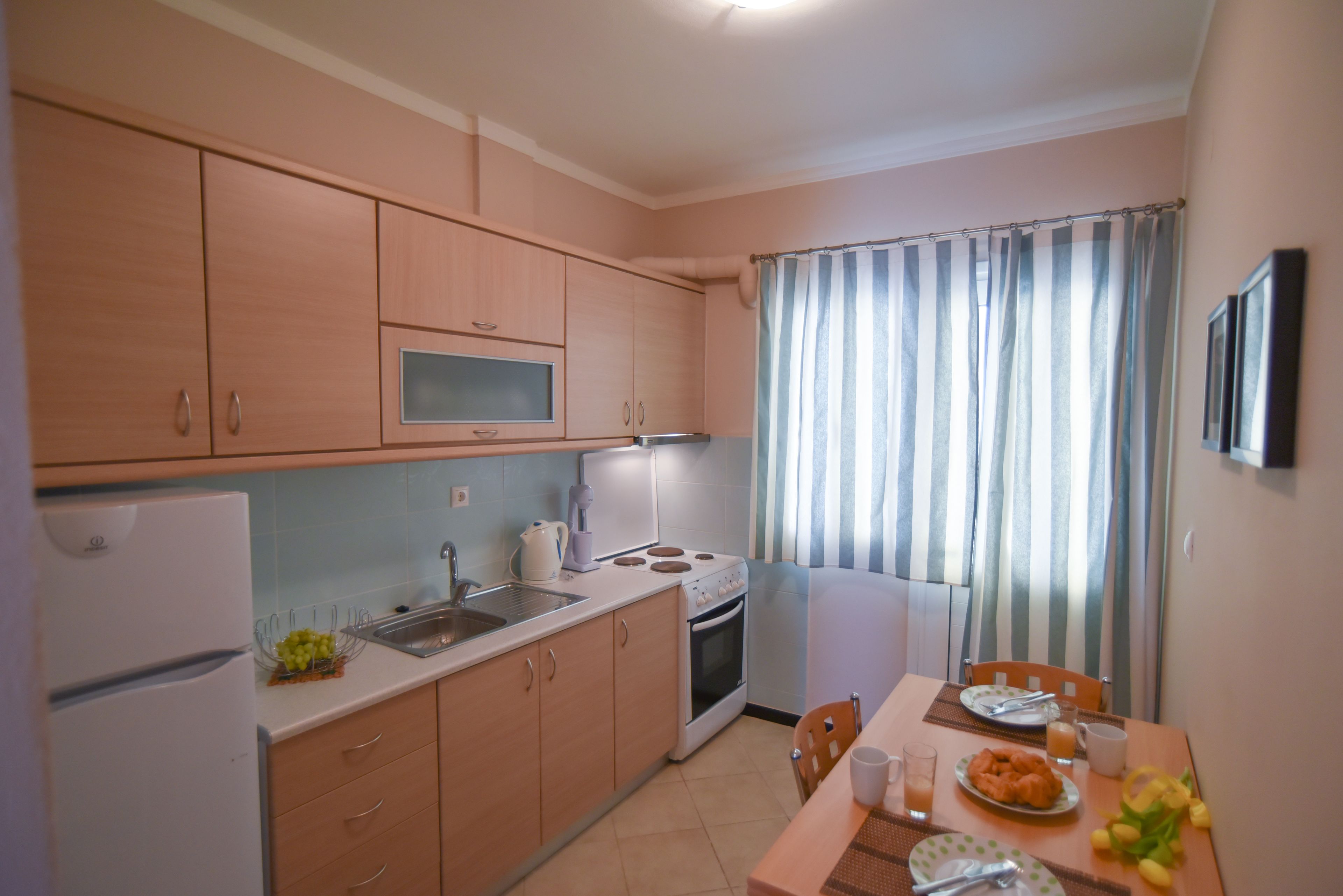 A compact kitchen with wooden cabinets, a refrigerator, a stove, and a dining area with a table set for two.