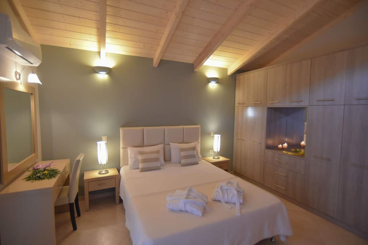 A hotel room with a bed, bedside lamps, a desk with a chair, a mirror, and a wardrobe.