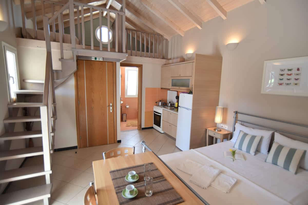 A bedroom with a bed, bedside table, and a view of the kitchen.