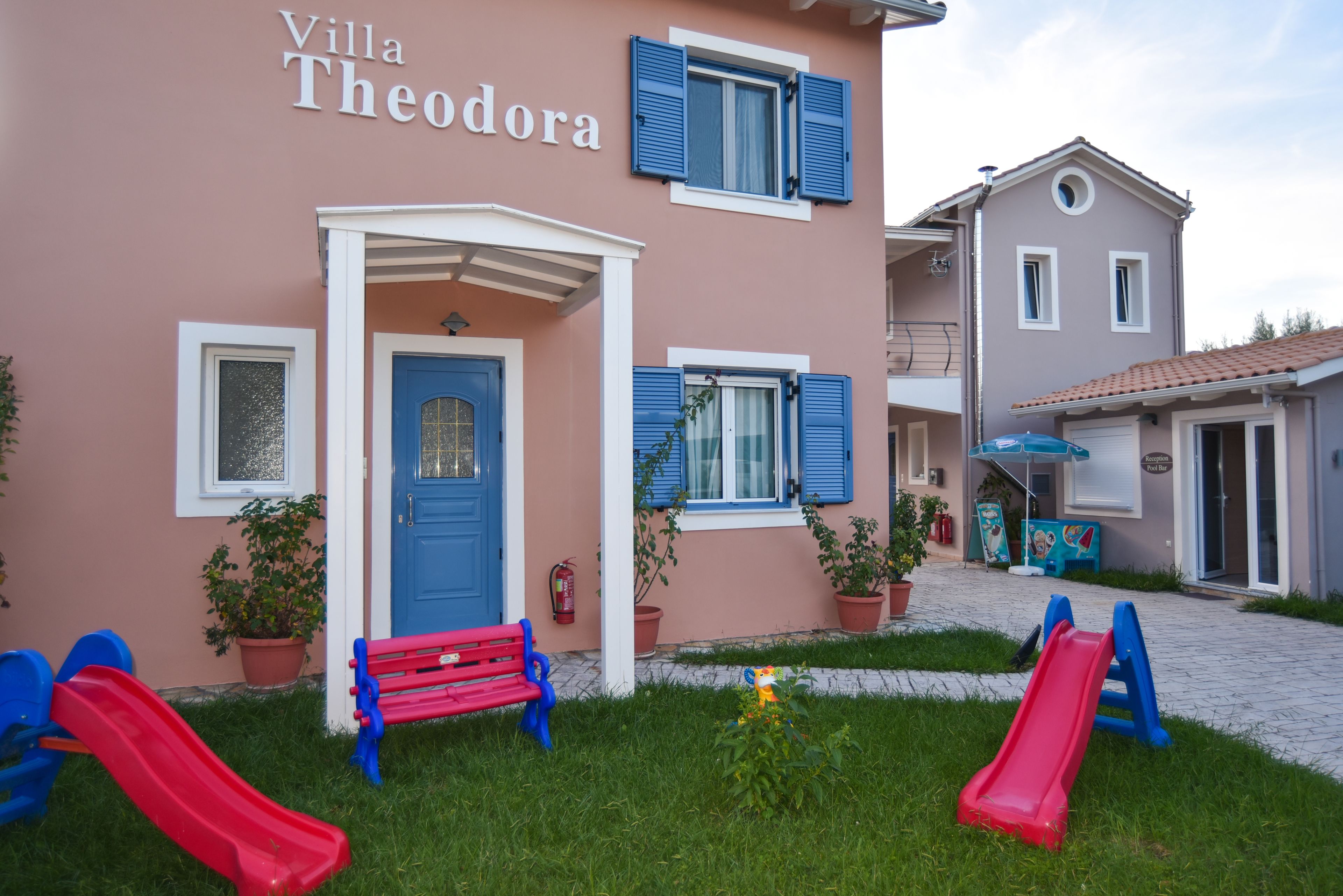 Villa Theodora with a blue door, two red slides, and a red bench.