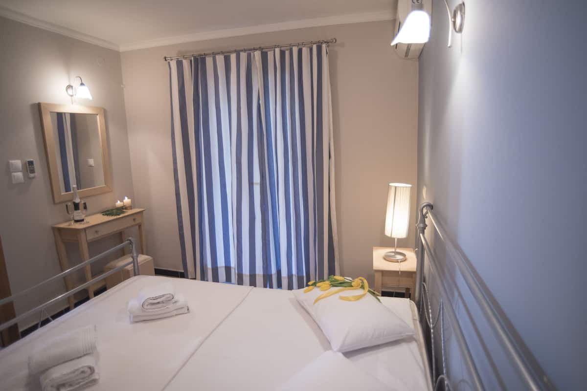 A hotel room with a bed, a bedside table, a lamp, a mirror, and a curtain.