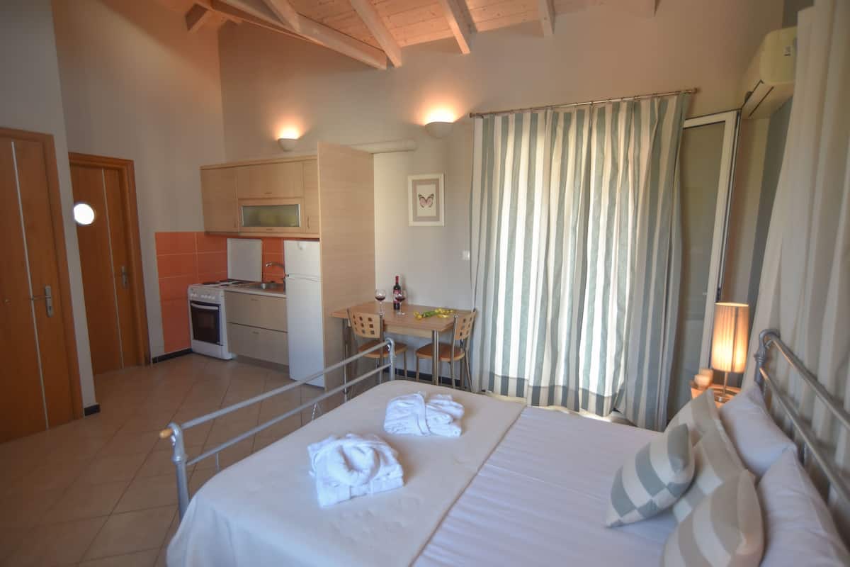 A hotel room with a bed, towels, a desk, a chair, a microwave, an oven, and a bathroom with a shower curtain.