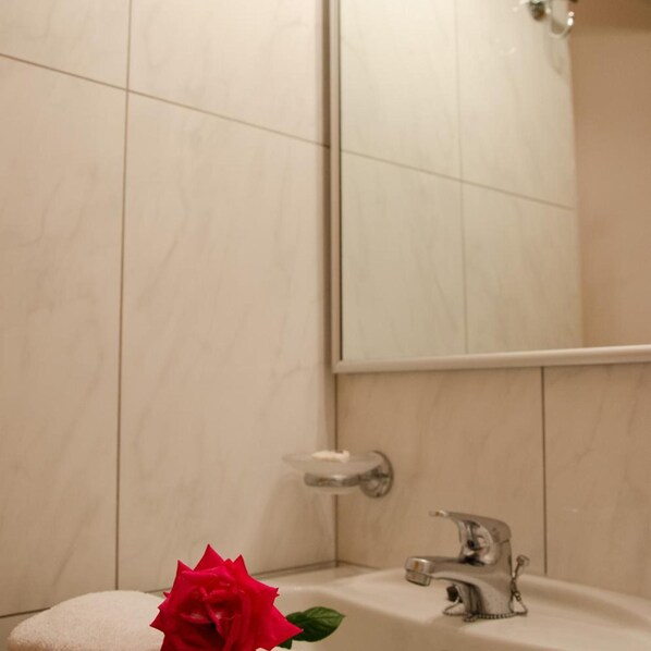 A bathroom with a white sink, a mirror, and a red rose on the counter. - Athos Hotel (Lefkada)