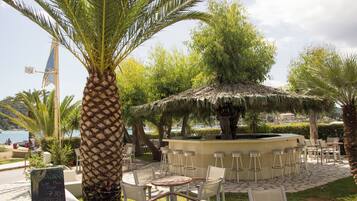 An outdoor seating area with a thatched-roof structure, surrounded by palm trees and chairs.