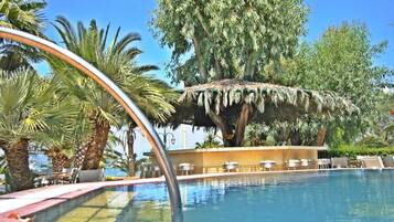 A pool area with lounge chairs, a thatched structure, and palm trees.