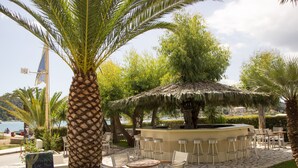 Un área de bar al aire libre con techo de paja, rodeada de palmeras y sillas.