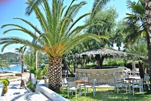 A seaside restaurant with outdoor seating, a bar, and a view of the sea. - Athos Hotel (Lefkada)