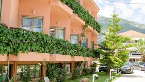 Un hotel de varios pisos con balcones cubiertos de vegetación, un camino pavimentado y un paisaje montañoso al fondo.