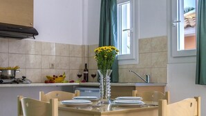 Comedor con una mesa de madera dispuesta para cuatro, un florero con flores amarillas y una ventana con cortinas verdes.