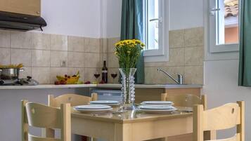 Comedor con una mesa de madera dispuesta para cuatro, un florero con flores amarillas y una ventana con cortinas verdes.