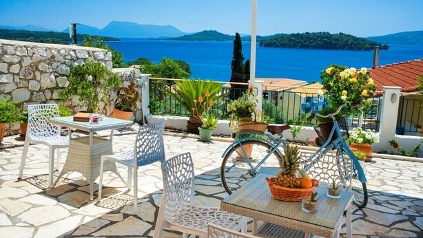 Una terraza con suelo de piedra, mobiliario de mimbre blanco y plantas en macetas.