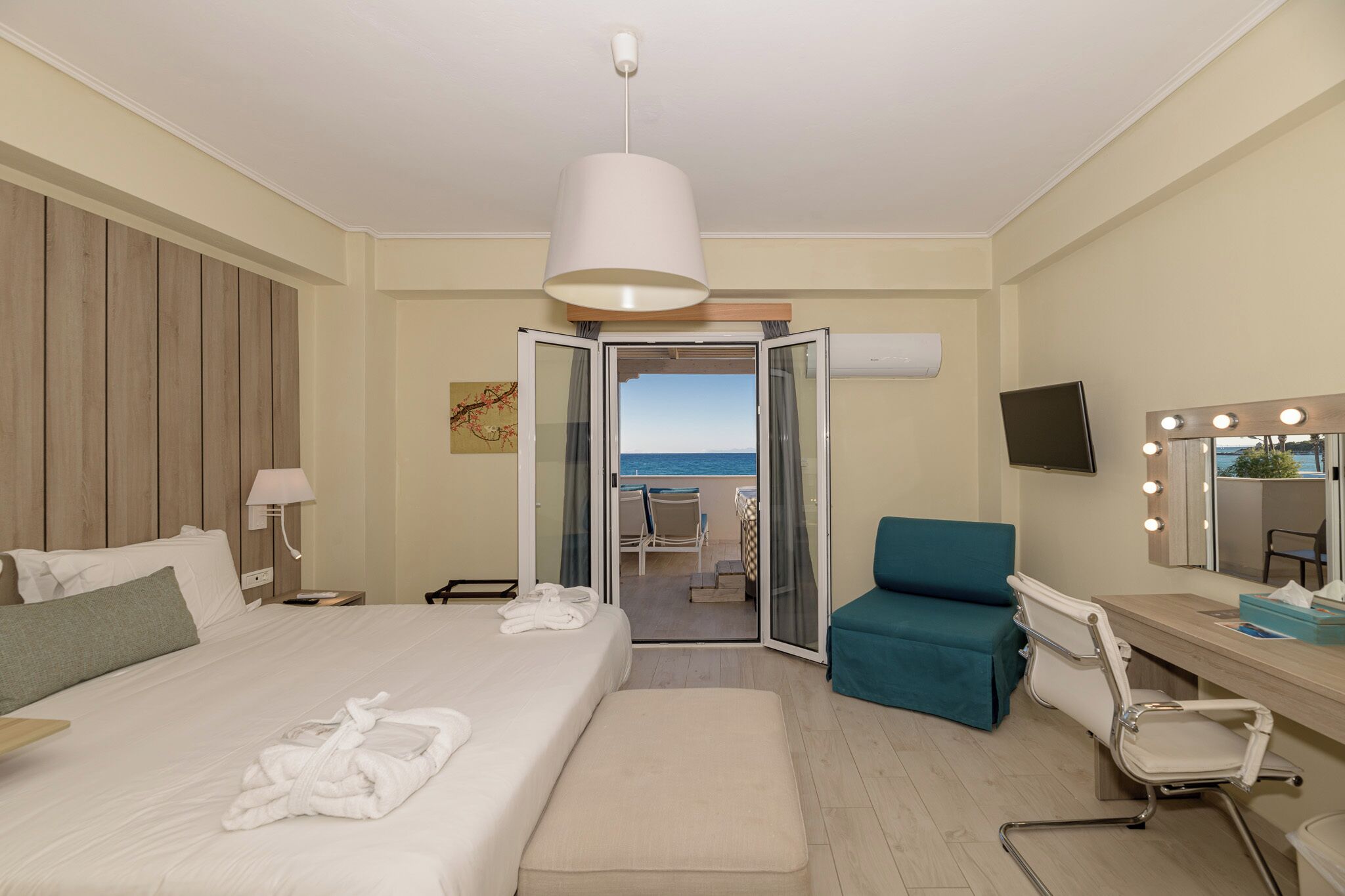 Een hotelkamer met een bed, een zithoek met uitzicht op zee, een kaptafel met verlichting en een televisie.