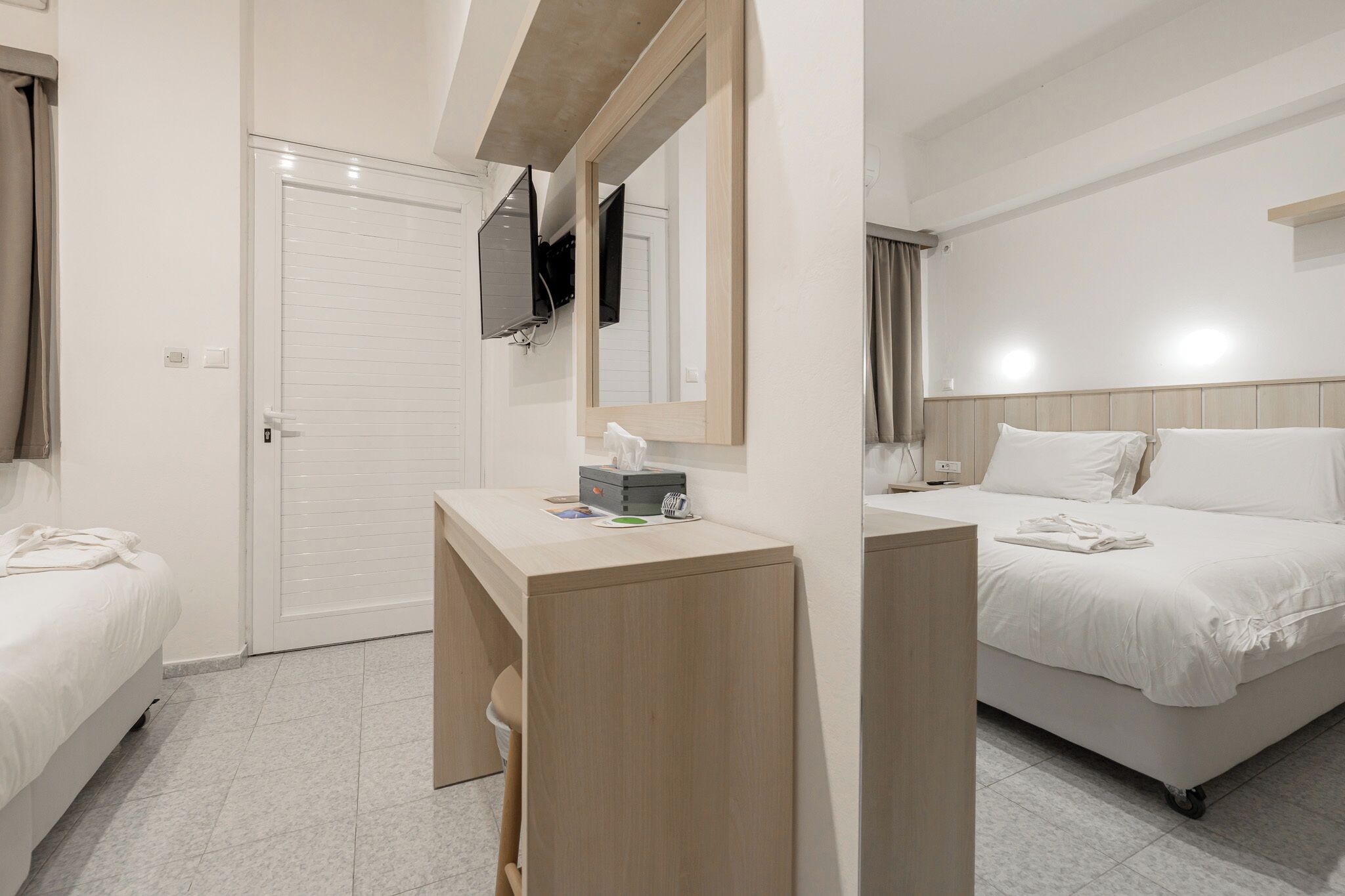 Habitación de hotel con cama, mesita de noche con espejo, televisor montado en la pared y puerta que da a un baño.