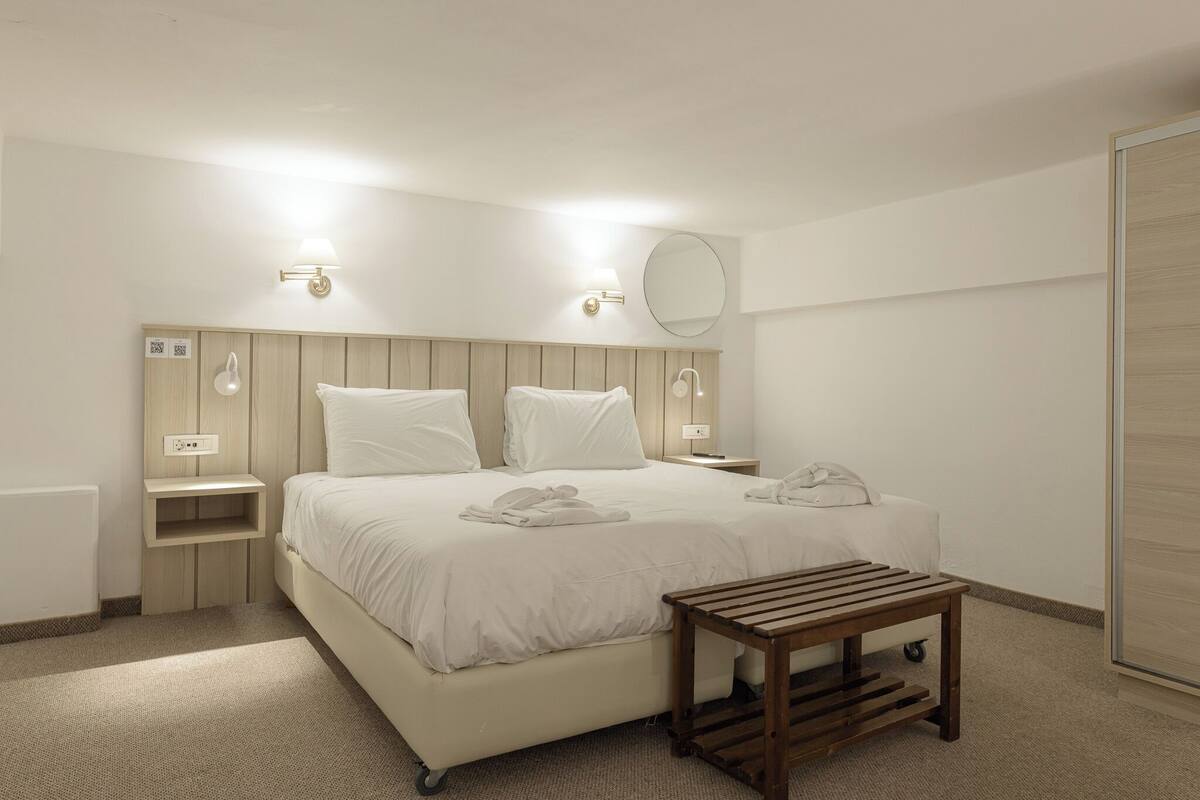 A modern hotel room with a large bed, bedside tables, a wooden bench, and a mirror.