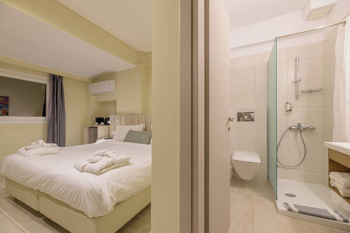 A hotel room with a bed, a bedside table, a shower with a glass door, and a toilet.