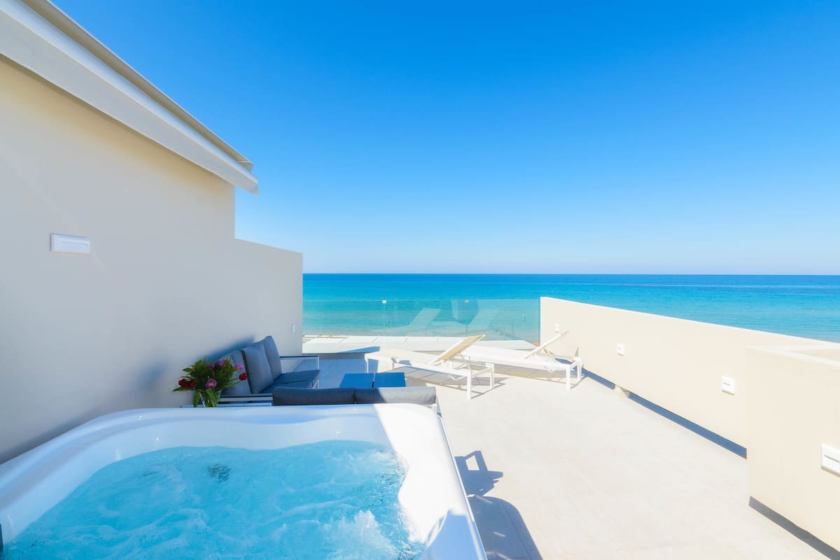 A rooftop terrace with a hot tub, lounge chairs, and a view of the ocean.