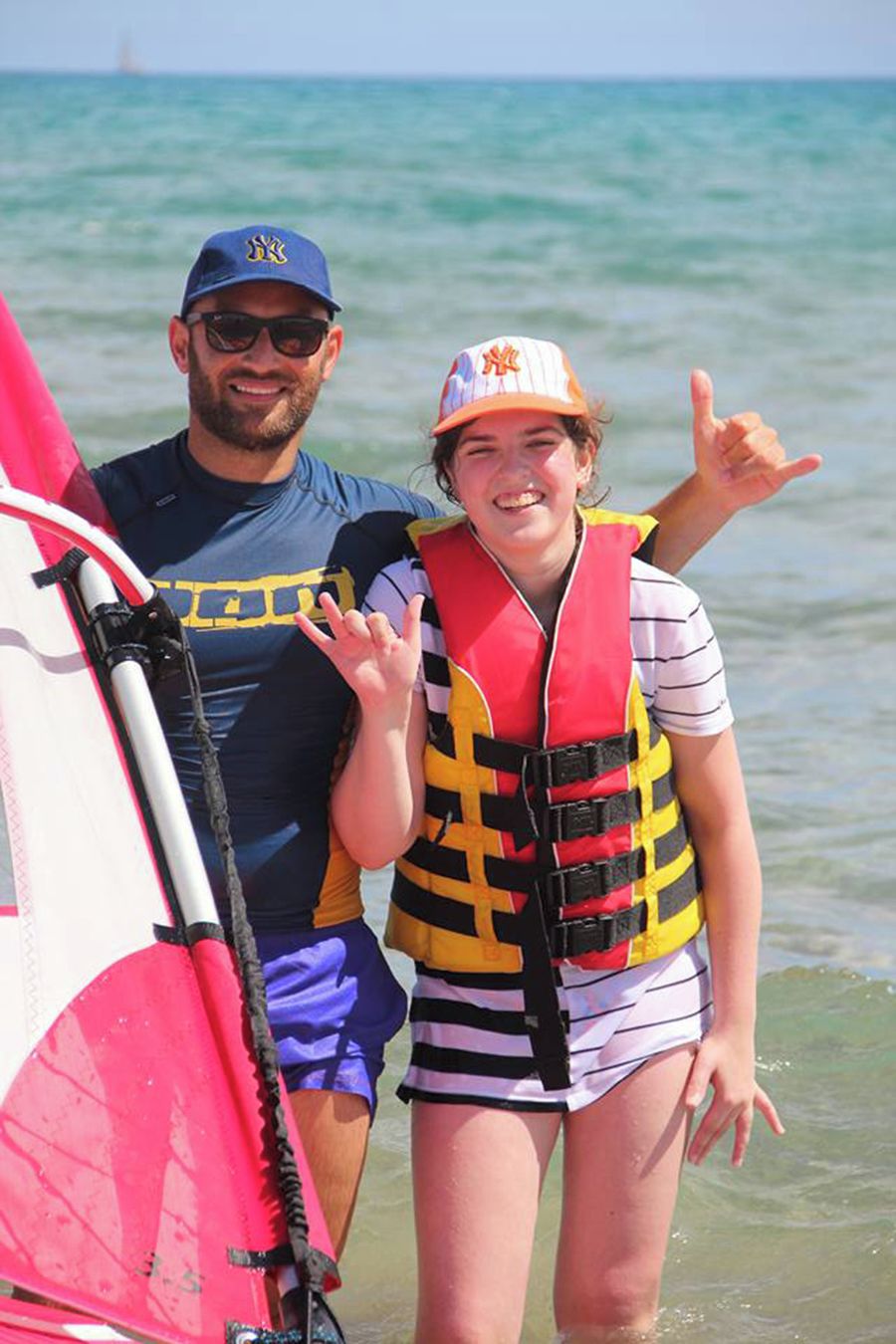 Dos personas junto a una tabla de surf en la playa.