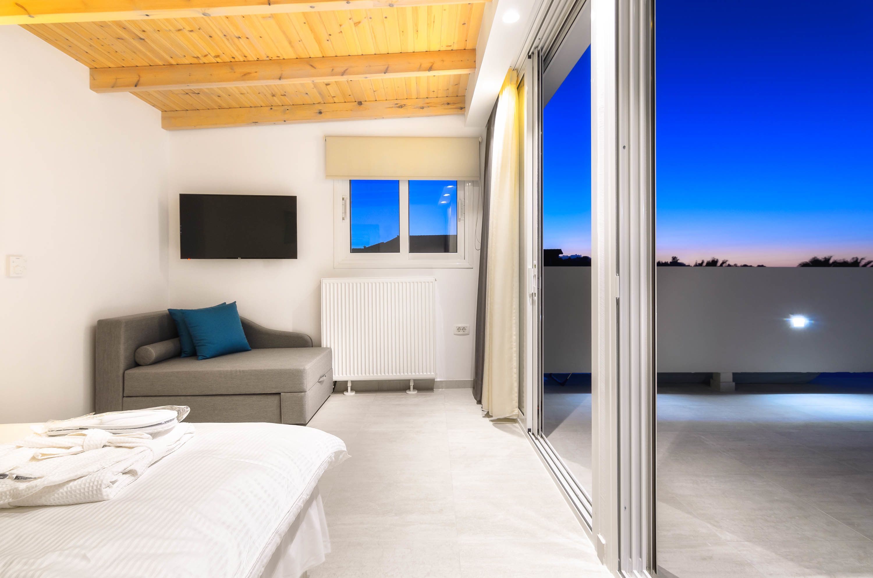 A modern bedroom with a bed, a sofa, a TV, and a view of the sky.